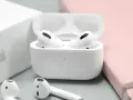 Białe słuchawki AirPods w etui, obok pudełka Apple i różowego notatnika.