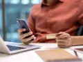 Dłoń trzymająca telefon i kartę kredytową przy laptopie.