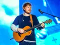 Ed Sheeran gra na gitarze akustycznej na tle niebieskiej sceny.