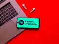 Laptop, telefon ze Spotify Premium i słuchawki na czerwonym tle.