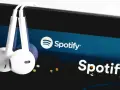 Białe słuchawki wiszą na ekranie smartfona z logo Spotify.
