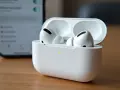 Białe słuchawki AirPods Pro w etui, obok wygaszonego ekranu telefonu.