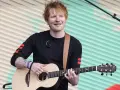 Ed Sheeran gra na gitarze akustycznej na tle pofalowanej, kolorowej kurtyny.