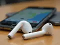 Białe słuchawki AirPods leżące obok smartfona z widoczną mapą.