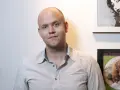 Daniel Ek, założyciel Spotify, w koszuli w paski na tle ściany z plakatami.