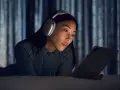 Kobieta w słuchawkach AirPods Max leży na łóżku i patrzy na tablet.