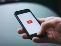 Dłoń trzymająca smartfon z logo YouTube.