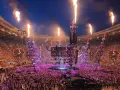 Koncert na stadionie z płomieniami, tłumem i sceną.
