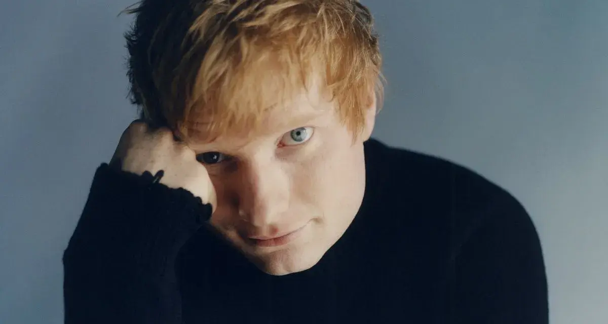 Ed Sheeran w czarnym golfie, opierający głowę na dłoni.