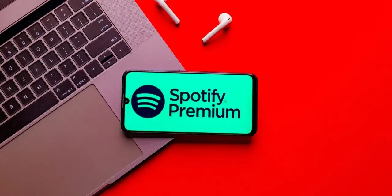 Laptop, telefon ze Spotify Premium i słuchawki na czerwonym tle.