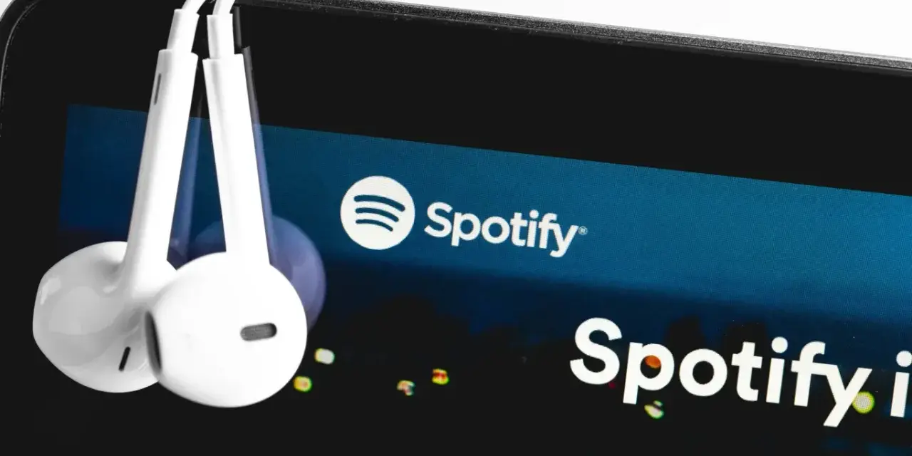 Białe słuchawki wiszą na ekranie smartfona z logo Spotify.