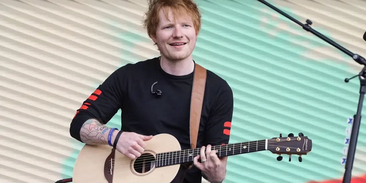 Ed Sheeran gra na gitarze akustycznej na tle pofalowanej, kolorowej kurtyny.
