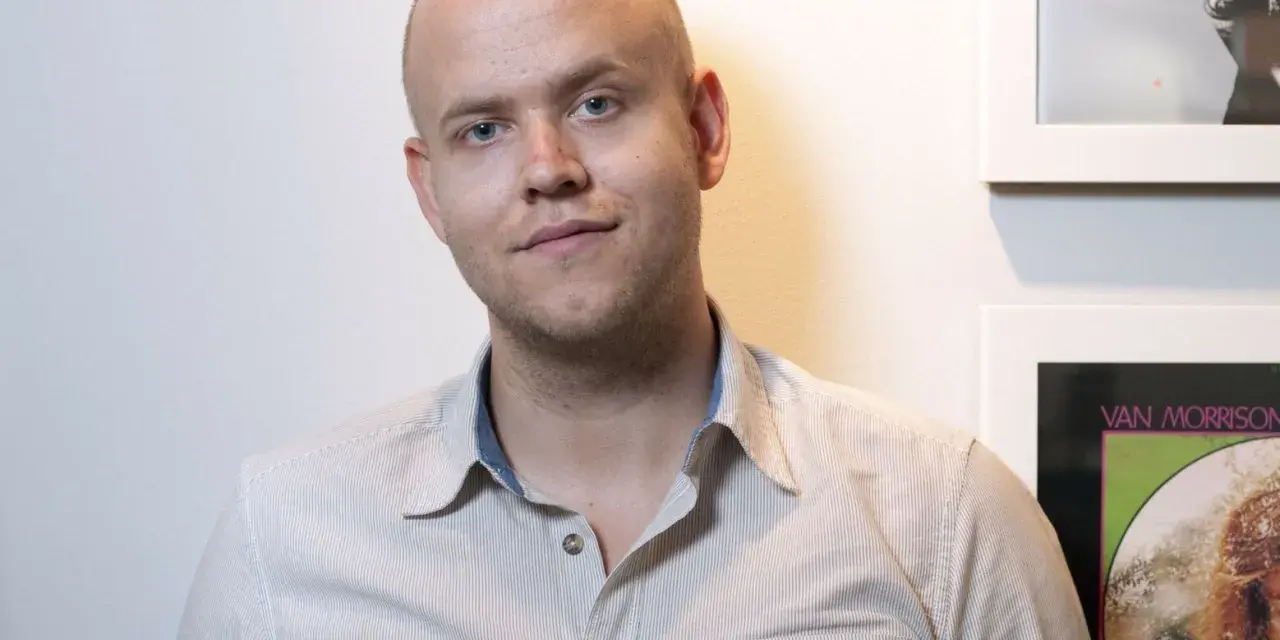 Daniel Ek, założyciel Spotify, w koszuli w paski na tle ściany z plakatami.