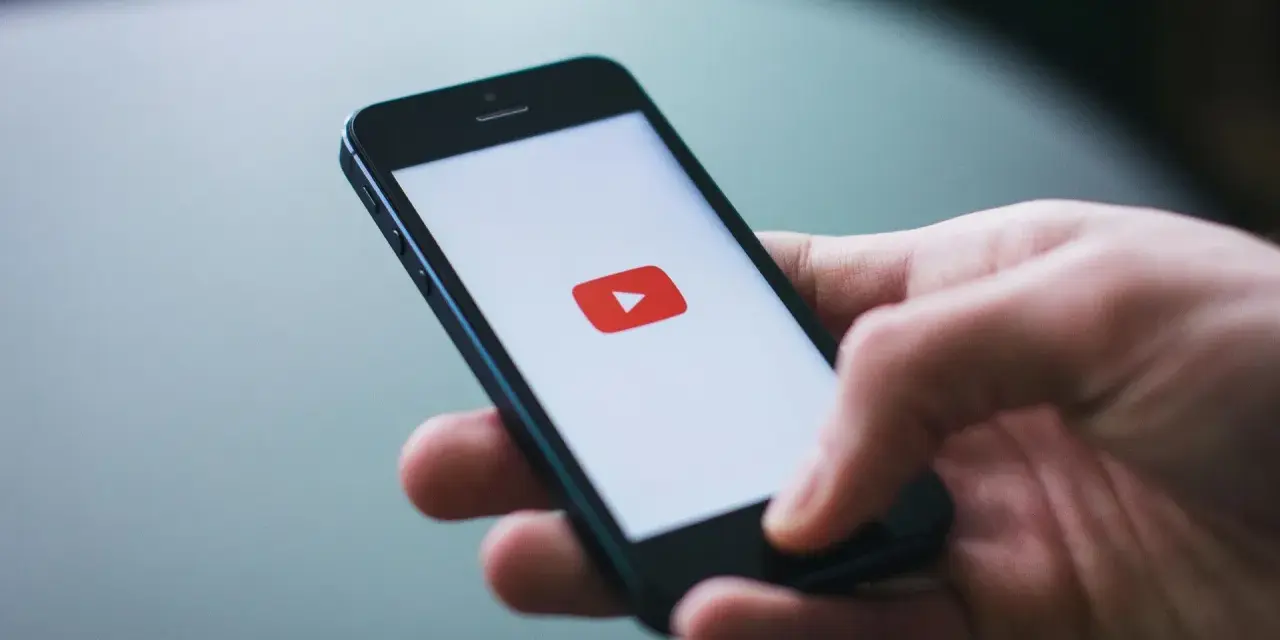 Dłoń trzymająca smartfon z logo YouTube.