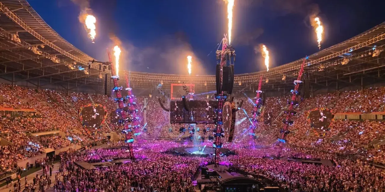 Koncert na stadionie z płomieniami, tłumem i sceną.