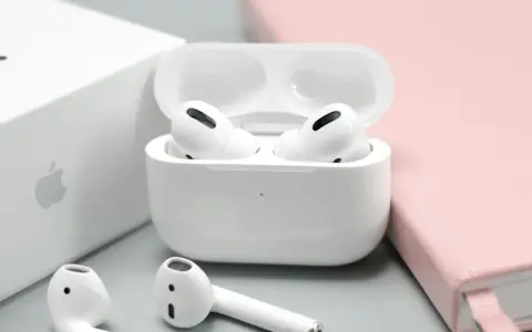 Białe słuchawki AirPods w etui, obok pudełka Apple i różowego notatnika.