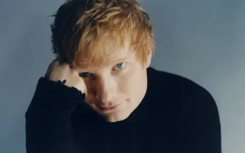 Ed Sheeran w czarnym golfie, opierający głowę na dłoni.