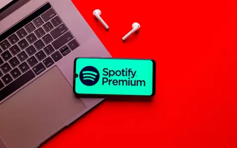 Laptop, telefon ze Spotify Premium i słuchawki na czerwonym tle.
