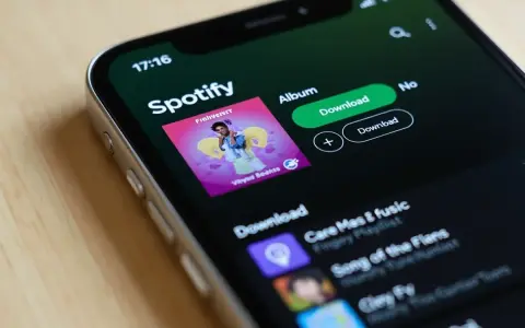 Ekran telefonu z aplikacją Spotify, widoczna okładka albumu i przyciski pobierania.