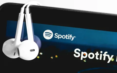 Białe słuchawki wiszą na ekranie smartfona z logo Spotify.