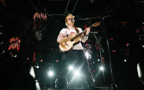 Ed Sheeran gra na gitarze na scenie w białej koszulce z polskim godłem.