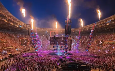 Koncert na stadionie z płomieniami, tłumem i sceną.