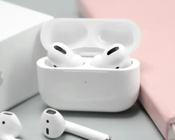 Białe słuchawki AirPods w etui, obok pudełka Apple i różowego notatnika.