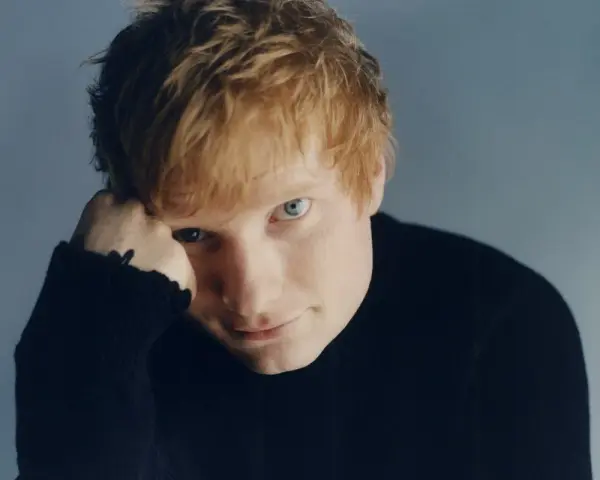 Ed Sheeran w czarnym golfie, opierający głowę na dłoni.