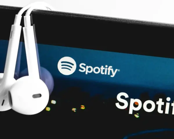 Białe słuchawki wiszą na ekranie smartfona z logo Spotify.