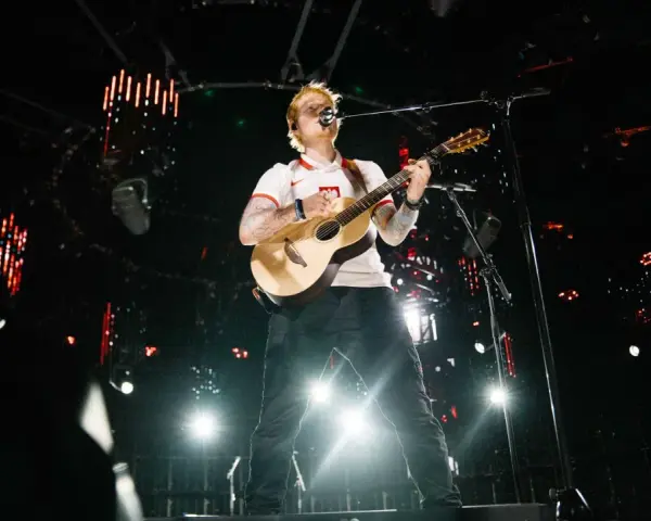 Ed Sheeran gra na gitarze na scenie w białej koszulce z polskim godłem.