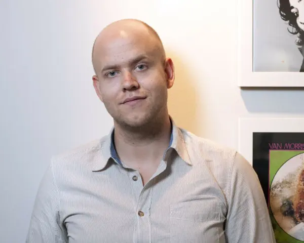 Daniel Ek, założyciel Spotify, w koszuli w paski na tle ściany z plakatami.