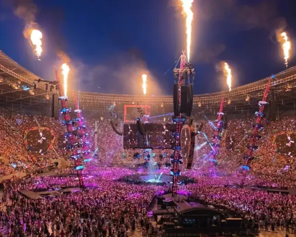 Koncert na stadionie z płomieniami, tłumem i sceną.