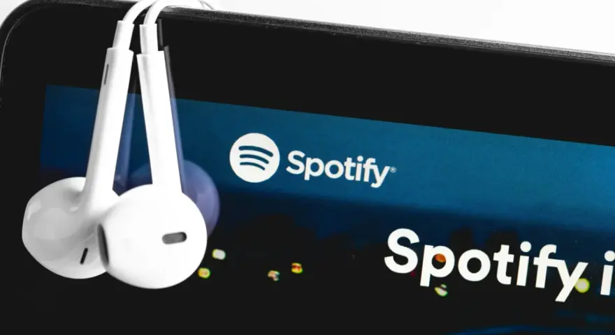 Białe słuchawki wiszą na ekranie smartfona z logo Spotify.