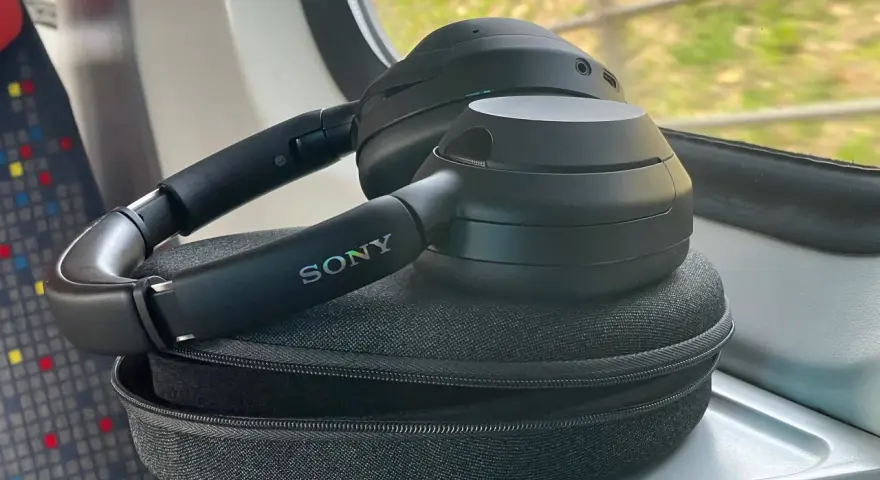 Czarne słuchawki Sony leżą na etui, na stoliku w pociągu.