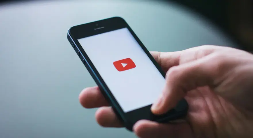 Dłoń trzymająca smartfon z logo YouTube.