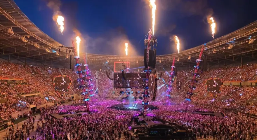 Koncert na stadionie z płomieniami, tłumem i sceną.